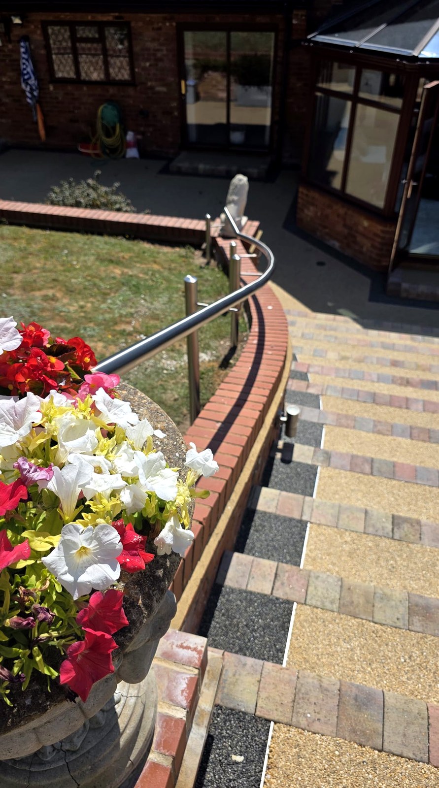 Stainless steel handrail posts with offset brackets set into the ground behind a brick wall, Beaconsfield
